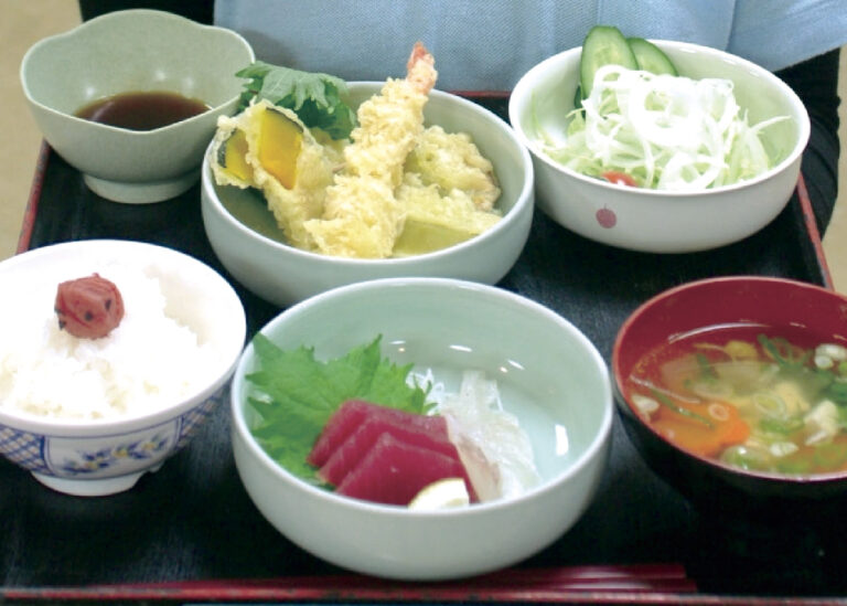 介護施設の食事。天ぷら、刺身、サラダ、ご飯、味噌汁が配置された定食セット